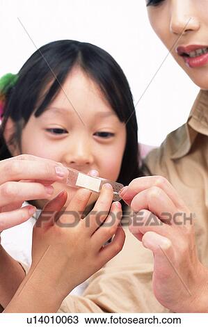 Stock Image -  a Mother applying adhesive bandage on her daughter's finger, Front View. Fotosearch