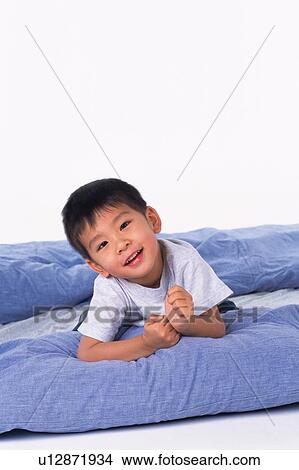 Boy lying on a Blue-colored feather mattress, looking at camera, Smiling, Front View View Large Photo Image Picture - Boy lying on a Blue-colored feather mattress, looking at camera, Smiling, Front View. Fotosearch