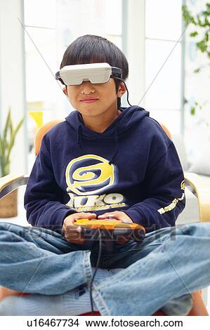 Boy playing a virtual reality game on a chair with his legs crossed, Front View View Large Photo Image Picture - Boy playing a virtual reality game on a chair with his legs crossed, Front View. Fotosearch