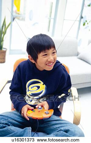 Boy playing video game on a chair with his legs crossed, Smiling, Looking Sideways, High Angle View View Large Photo Image Stock Image - Boy playing video game on a chair with his legs crossed, Smiling, Looking Sideways, High Angle View. Fotosearch