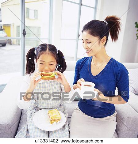 Girl Eating a Sandwich While Sitting on a Sofa, Mother Having a Cup of Coffee Next to her, High Angle View, Differential Focus View Large Photo Image Stock Image - Girl Eating a Sandwich While Sitting on a Sofa, Mother Having a Cup of Coffee Next to her, High Angle View, Differential Focus. Fotosearch