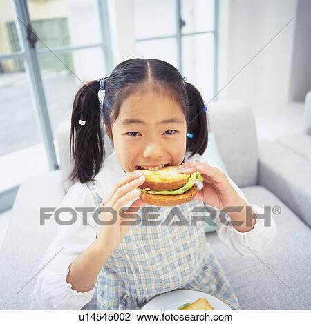 Girl eating a sandwich While sitting on a sofa, looking at camera, Smiling, High Angle View, Differential Focus View Large Photo Image Stock Image - Girl eating a sandwich While sitting on a sofa, looking at camera, Smiling, High Angle View, Differential Focus. Fotosearch
