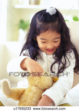 Stock Image - Girl holding and playing with a teddy bear Looking Down, Smiling, High Angle View, Differential Focus . Fotosearch