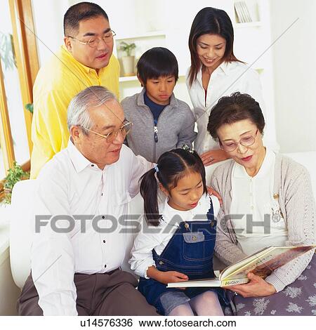 Stock Photograph - Japanese family in living room looking at photo album together, High Angle View, Front View. Fotosearch