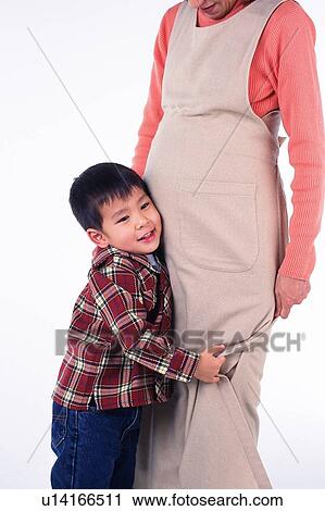 Stock Image - Little Boy putting his ear on the stomach of his pregnant mother, Smiling, Side View. Fotosearch