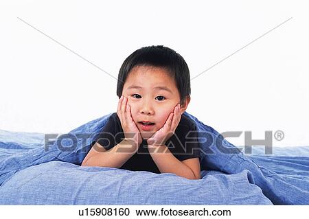 Stock Image - Little Boy resting his chin on his hands Under a Blue Blanket, looking at camera, Front View. Fotosearch