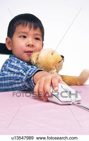 Stock Photo - Little Boy using a computer mouse and holding a teddy bear, Low Angle View, Side View. Fotosearch