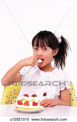 Stock Photography - Little Girl eating a strawberry cake at the Table, Looking Sideways, Front View. Fotosearch