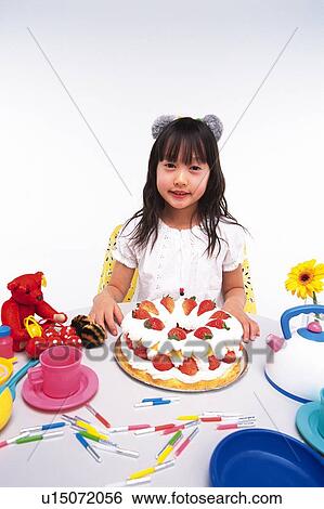 Stock Photograph - Little Girl sitting at a table with a birthday cake and some kitchenware, looking at camera, Smiling, High Angle View. Fotosearch