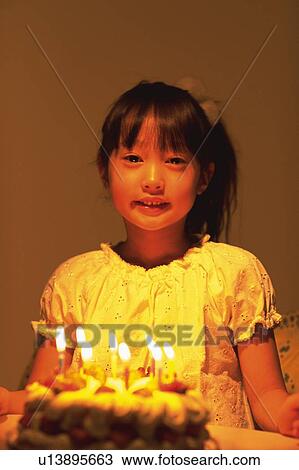 Stock Image - Little Girl sitting in front of a birthday cake with burning candles, Looking at Camera, Smiling, Front View, Differential Focus. Fotosearch