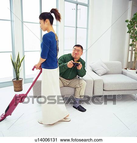Mid Adult Man Playing a Video Game Being Distracted by His Vacuuming wife, Side View View Large Photo Image Stock Image - Mid Adult Man Playing a Video Game Being Distracted by His Vacuuming wife, Side View. Fotosearch