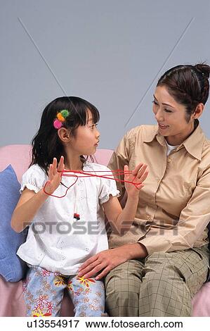 Stock Photo - Mother and daughter looking at each other, daughter playing cat's cradle, sitting on the sofa, Front View. Fotosearch