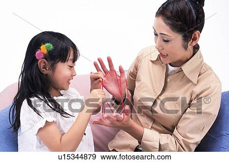 Stock Photo - Mother and daughter playing cat's cradle, sitting on a sofa, Side View. Fotosearch