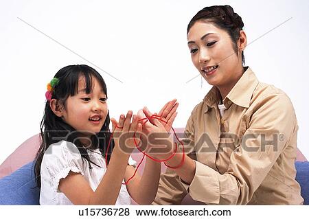 Stock Photo - Mother and daughter playing cat's cradle While Sitting on a sofa, Smiling, Front View. Fotosearch
