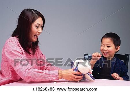 Stock Image - Mother and son playing with a teddy bear at the Table, Smiling, Side View. Fotosearch