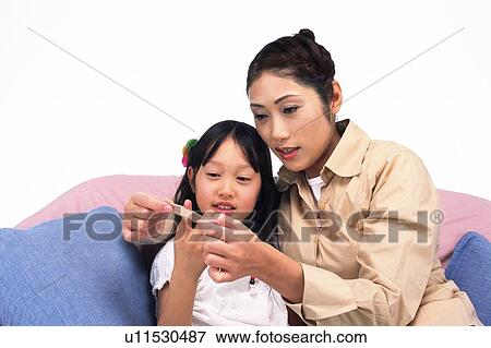 Stock Photo - Mother applying an adhesive bandage on her daughter's finger, Sitting on a Sofa, Front View. Fotosearch
