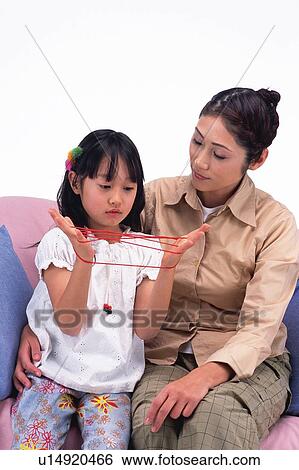 Mother looking at daughter who's playing cat's cradle, sitting on the sofa, Front View View Large Photo Image Stock Photograph - Mother looking at daughter who's playing cat's cradle, sitting on the sofa, Front View. Fotosearch