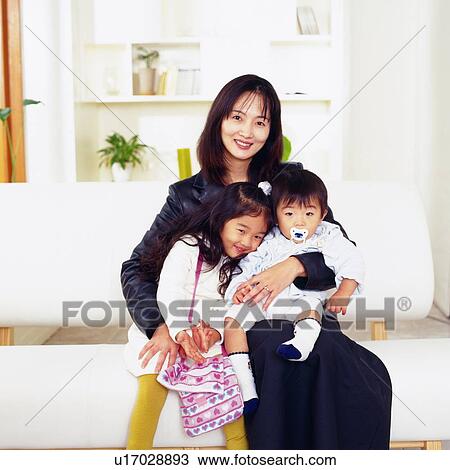 Stock Image - Portrait of a mother and her two children Sitting on a Sofa, Smiling, Front View. Fotosearch