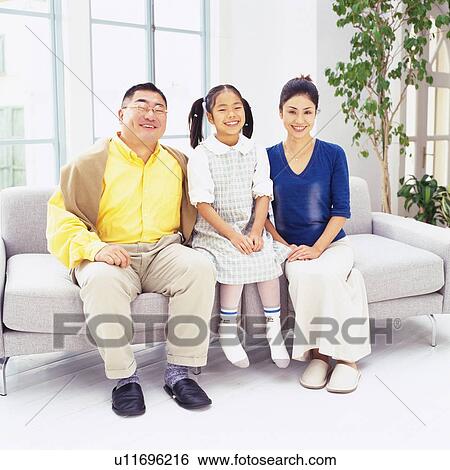 Portrait of parents and their daughter Sitting on a Couch in the Living Room, Smiling, Front View View Large Photo Image Stock Photograph - Portrait of parents and their daughter Sitting on a Couch in the Living Room, Smiling, Front View. Fotosearch