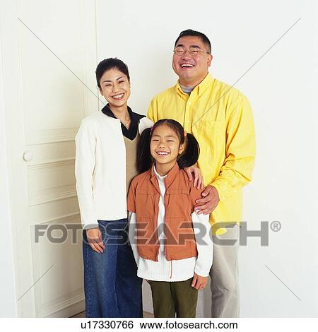Stock Photograph - Portrait of parents and their daughter In Front of a White Wall, Looking at Camera, Smiling, Front View. Fotosearch