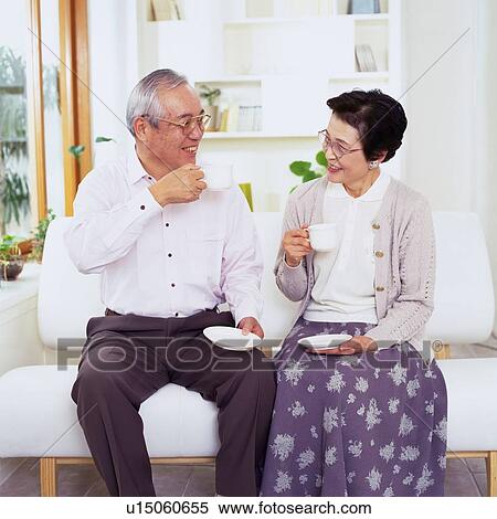 Senior Couple Drinking a Cup of Coffee While Sitting on a Sofa, Smiling, Looking at Each Other, Front View View Large Photo Image Stock Photography - Senior Couple Drinking a Cup of Coffee While Sitting on a Sofa, Smiling, Looking at Each Other, Front View. Fotosearch