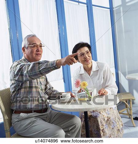 Stock Photograph - Senior Couple Having a Cup of Coffee in a caf?, the man Pointing at Something, Low Angle View. Fotosearch