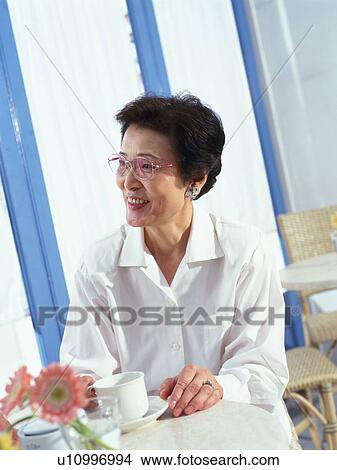 Picture - Senior woman smiling while Having a Cup of Coffee, Looking Sideways, Sitting by window, Low Angle View. Fotosearch