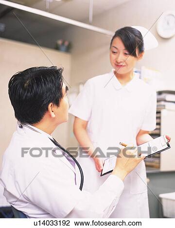 Stock Image - Doctor and nurse talking about a clipboard. Fotosearch