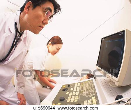 Picture - Doctor examining to use a machine, nurse standing nearby. Fotosearch