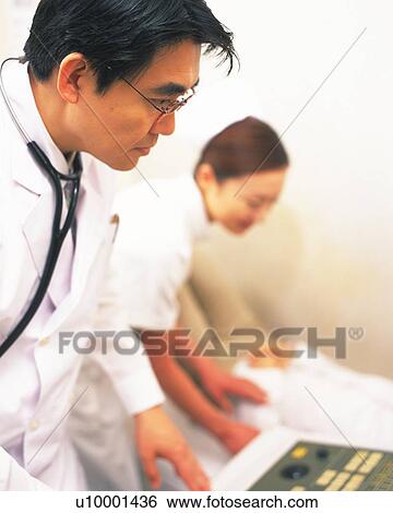 Stock Photograph - Doctor examining to use a machine, nurse standing nearby. Fotosearch