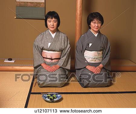 Stock Image - Two women sitting on Tatami mat in a tea room, front view, Japan. Fotosearch