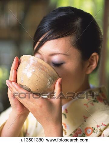 Stock Image - Woman in kimono drinking a cup of tea at tea ceremony, close up, Japan, differential focus. Fotosearch