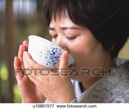 Stock Photo - Woman in kimono drinking a cup of tea at tea ceremony, close up, Japan, differential focus. Fotosearch