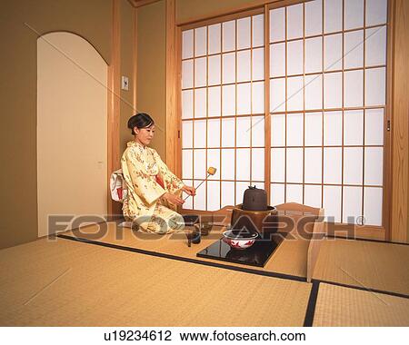Stock Image - Woman in kimono holding a bamboo dipper in a tea room, side view, Japan. Fotosearch