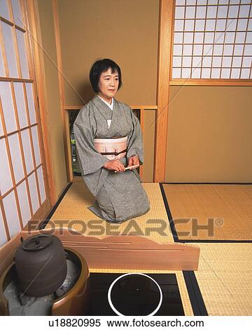 Stock Photography - Woman in kimono holding a Japanese folding fan and sitting on Tatami mat, front view, Japan. Fotosearch
