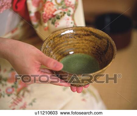Stock Image - Woman in kimono holding a tea cup at tea ceremony, high angle view, close up, Japan, differential focus. Fotosearch