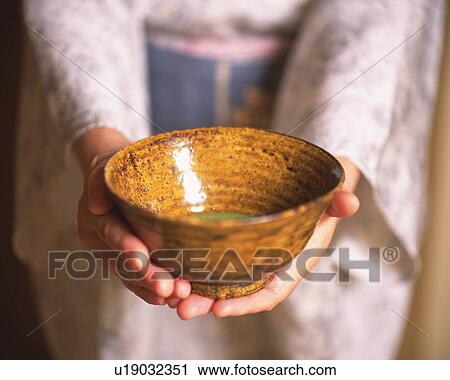 Stock Image - Woman in kimono holding a tea cup at tea ceremony, front view, close up, Japan, differential focus. Fotosearch