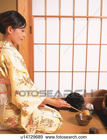 Stock Photo - Woman in kimono pouring hot water in a tea cup, side view, Japan. Fotosearch