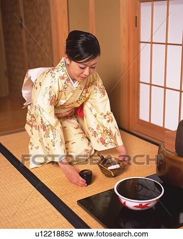 Stock Image - Woman in kimono setting up tea set for tea ceremony, high angle view, Japan. Fotosearch