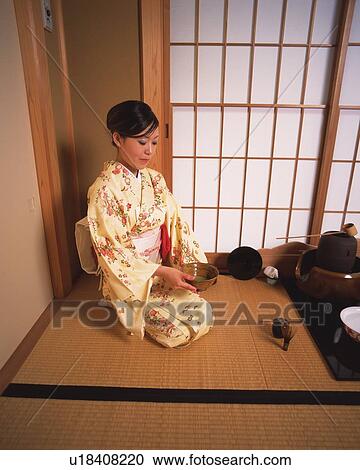 Stock Image - Woman in kimono sitting and holding a cup of tea in a tea room, high angle view, Japan. Fotosearch