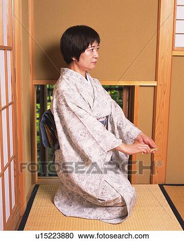 Stock Image - Woman in kimono sitting on Tatami mat, side view, Japan. Fotosearch