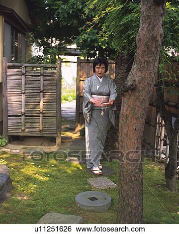 Stock Photograph - Woman in kimono standing in Japanese garden, front view, Japan. Fotosearch