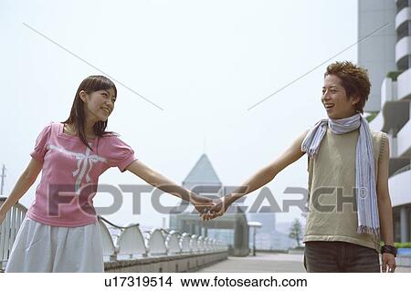 Picture - Young couple holding hands while walking, smiling . Fotosearch