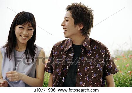 Stock Photograph - Young couple sitting in field of grass. Fotosearch