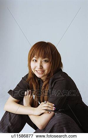 Stock Photo - Young woman hugging knees, looking up, smiling, crossing arms. Fotosearch