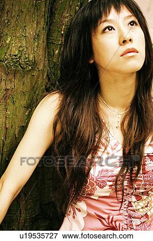 Stock Photo - Young woman leaning against tree. Fotosearch