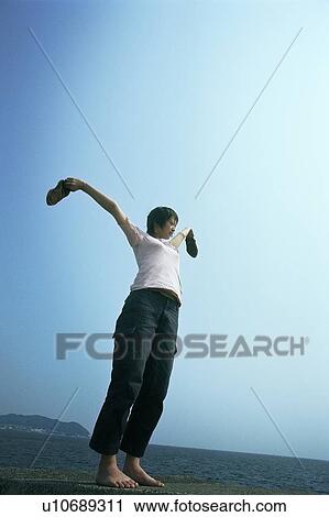 Stock Image - Young woman standing in field of grass with open arms. Fotosearch