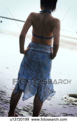 Stock Photo - Young women standing at the water edge, rear view. Fotosearch