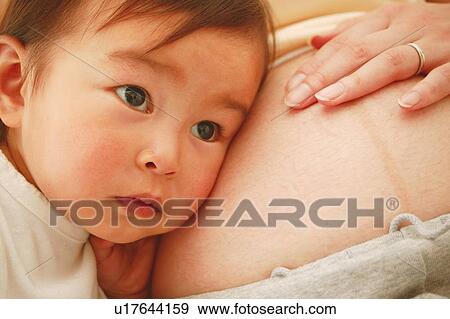 Stock Photo - A Baby Girl put her cheeks on to mothers pregnant stomach. Fotosearch