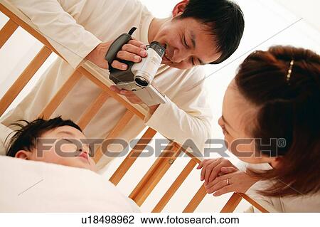 Parents filming their baby over the baby bed View Large Photo Image Stock Image - Parents filming their baby over the baby bed. Fotosearch